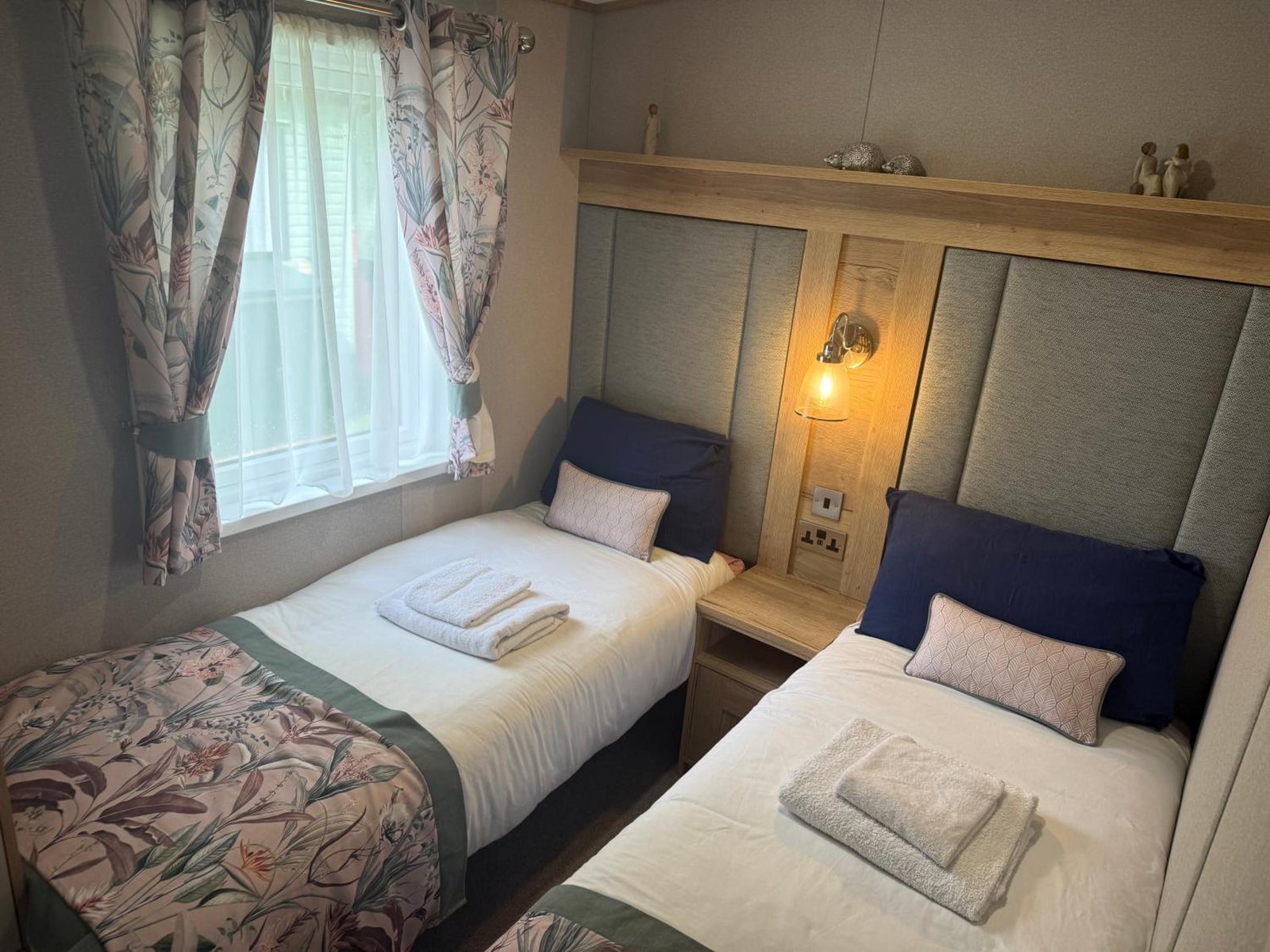 A twin room: two single beds, a sage headboard and a lit wall lamp