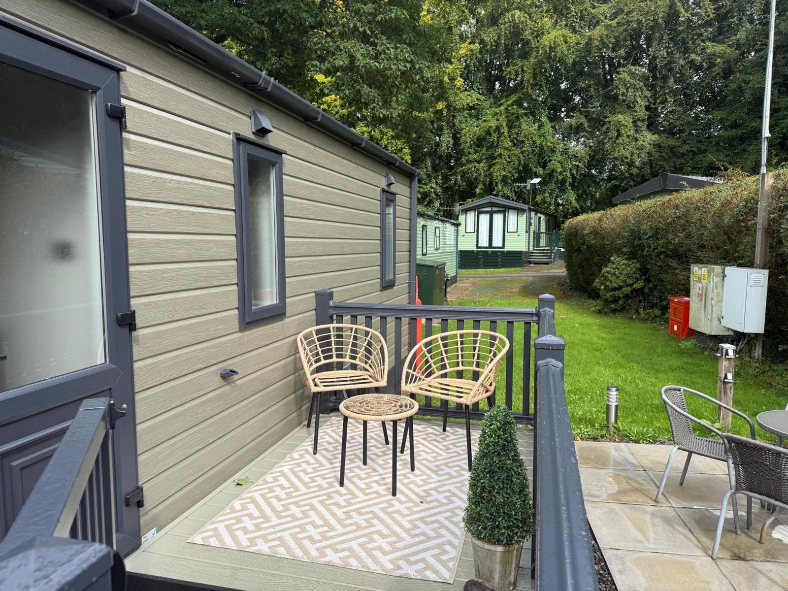 The side deck: two rattan chairs and a low table on a patterned rug against olive cladding